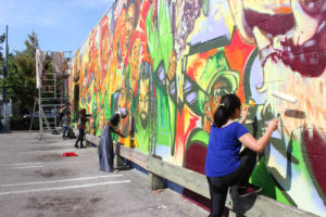Community members painting a large, colourful mural in Toronto's Little Jamaica