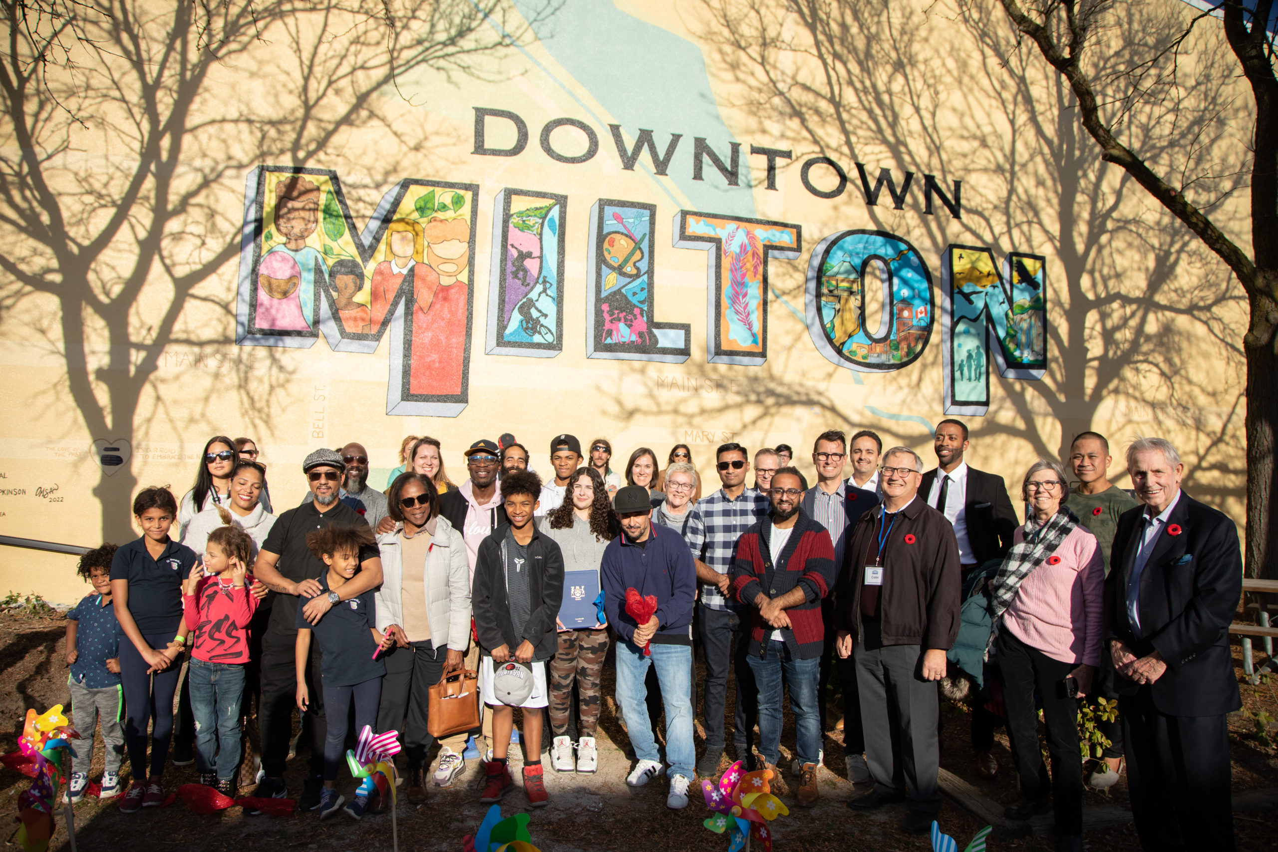 Community members gathered for a group photo in front of a Downtown Milton mural
