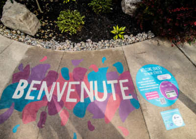 A ground mural by Bareket Kezwer that says BENVENUTE in white block letters and blue, pink and purple organic blobs around it