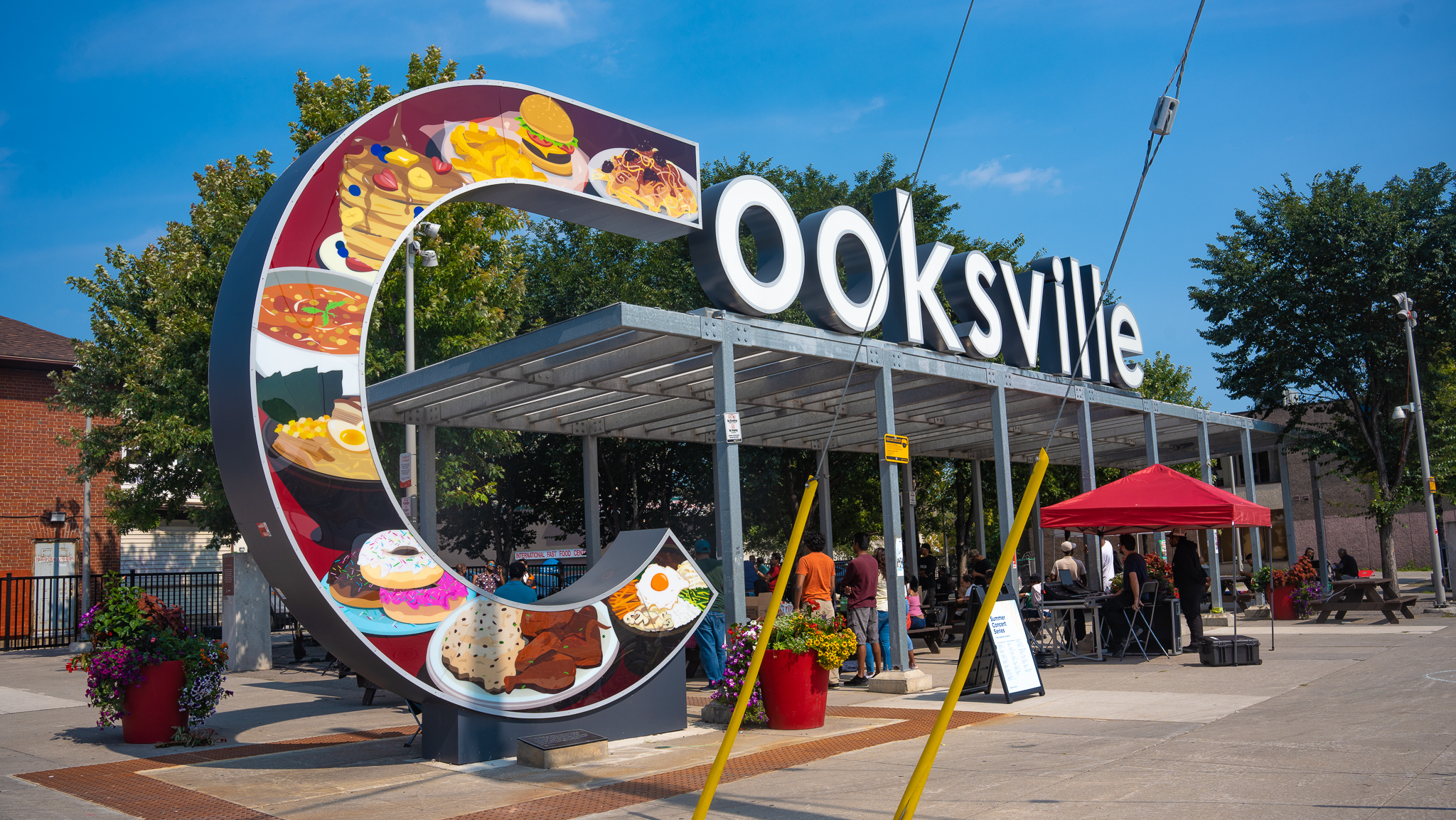 Photograph of the Cooksville sign with a food illustration by Ashley Mozo in the 'C'.