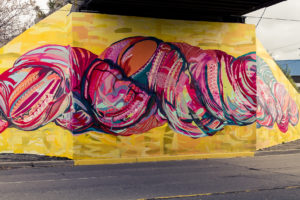 A yellow and pink section of the SKEIN Dufferin Beltline Underpass mural in Toronto