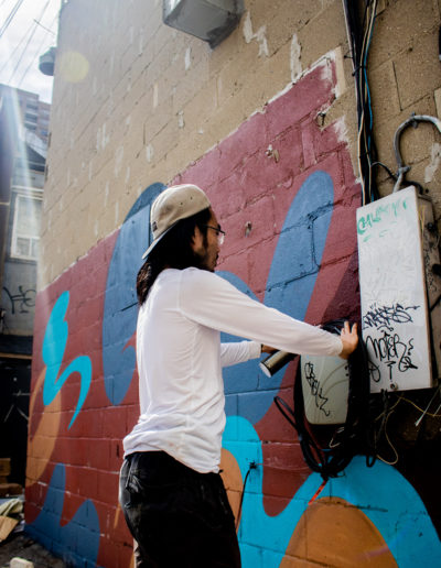 Photo of artist Andre Kan painting a geometric mural with red, blue and orange colours, he is wearing a white shirt and black pants