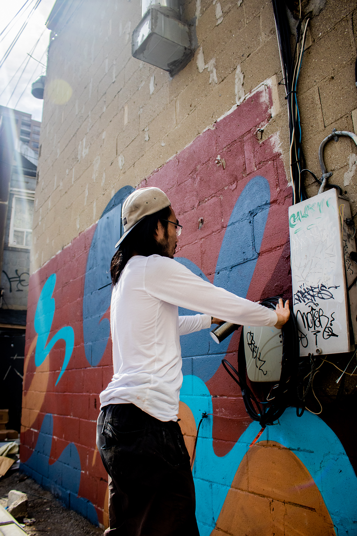 Photo of artist Andre Kan painting a geometric mural with red, blue and orange colours, he is wearing a white shirt and black pants