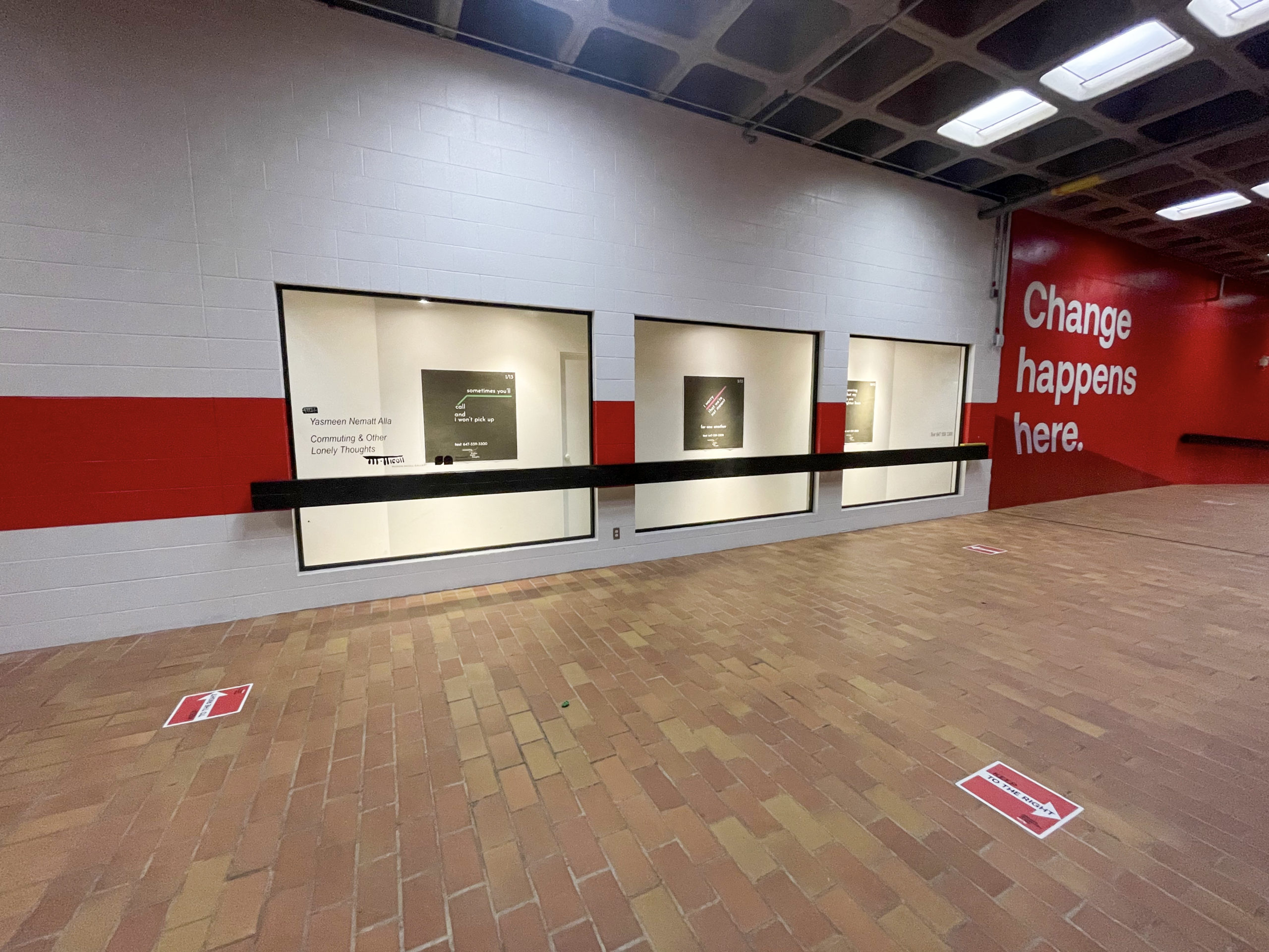 Photo of Yasmeen Nematt Alla's poster installation at Marion Nicoll Gallery in Alberta. The wall is while with a painted red stripe, and brown tile floor