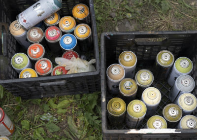 Photo of two black crates of colourful spray paints sitting on the grass.