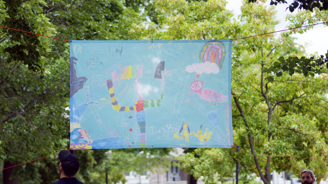 Banner hanging in a park and created by CreateSpace 2021 artist Anna Jane McIntyre in collaboration with elementary school children in Montreal
