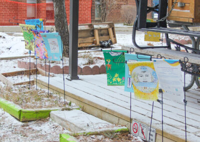 Weaving Our Roots flag garden on a snowy day. There are colourful designs created by the community with green, yellow and teal colours used throughout.
