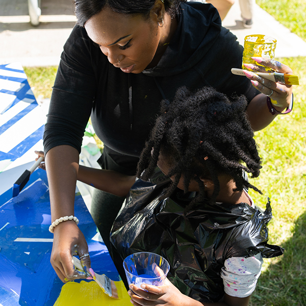An action shot shows participants painting at From Weeds We Grow events