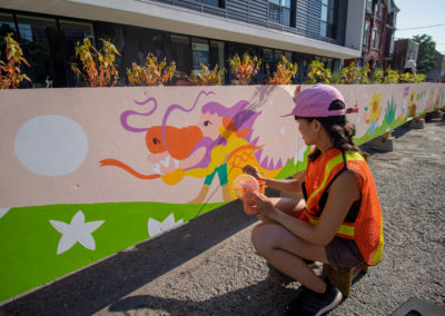 Justine Wong painting an outdoor mural of a dragon on a parkette.