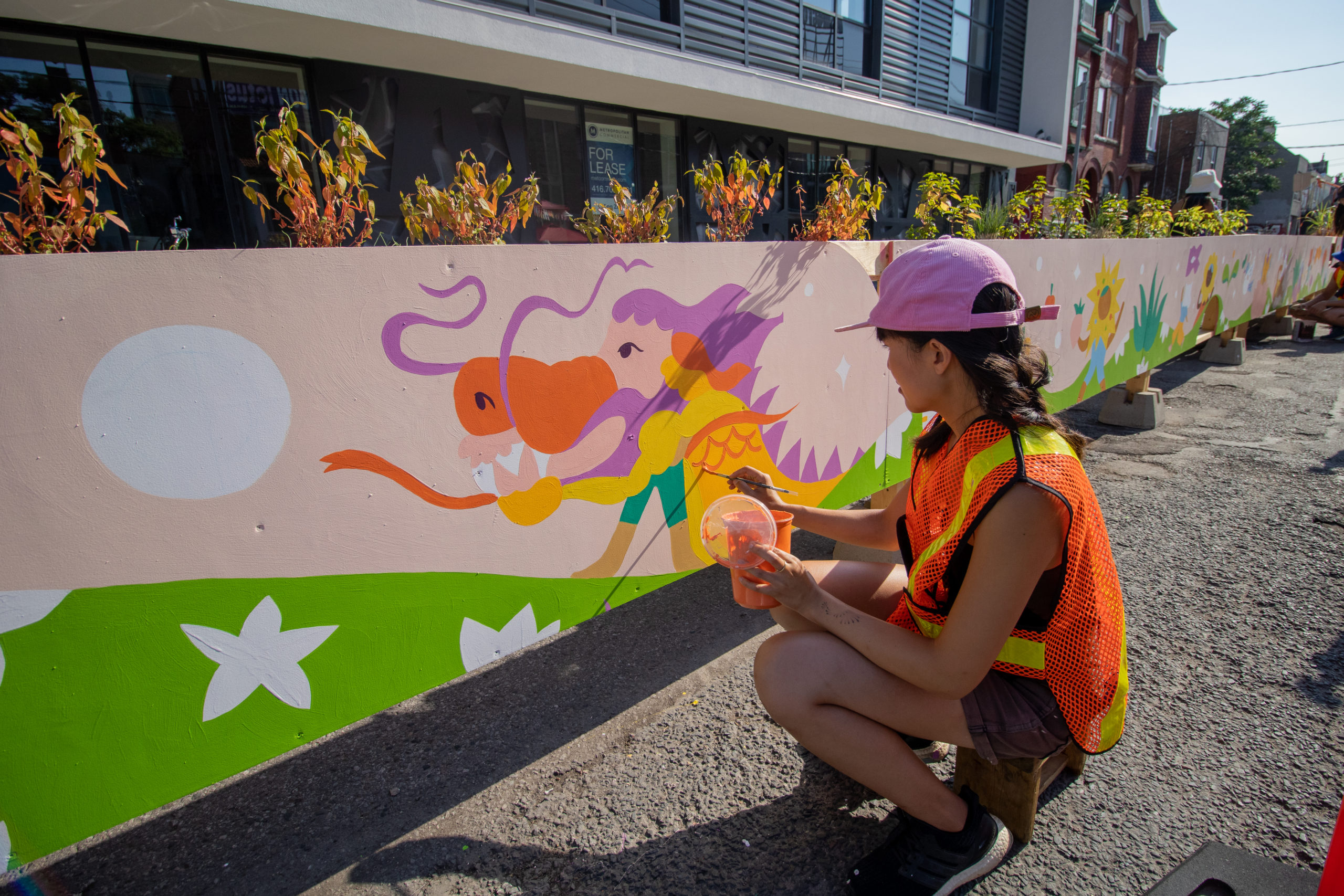 Justine Wong painting an outdoor mural of a dragon on a parkette.