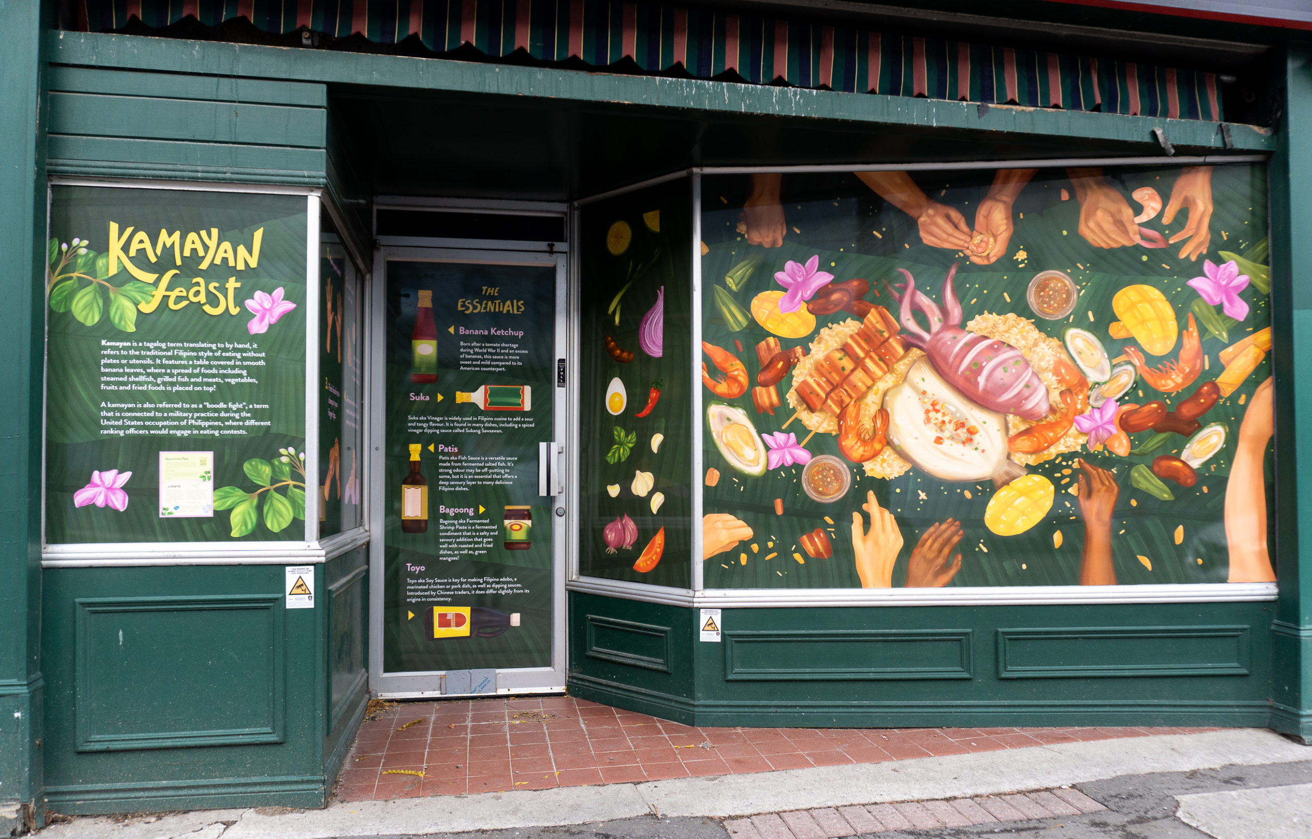 A green storefront with large window mural of illustrated food