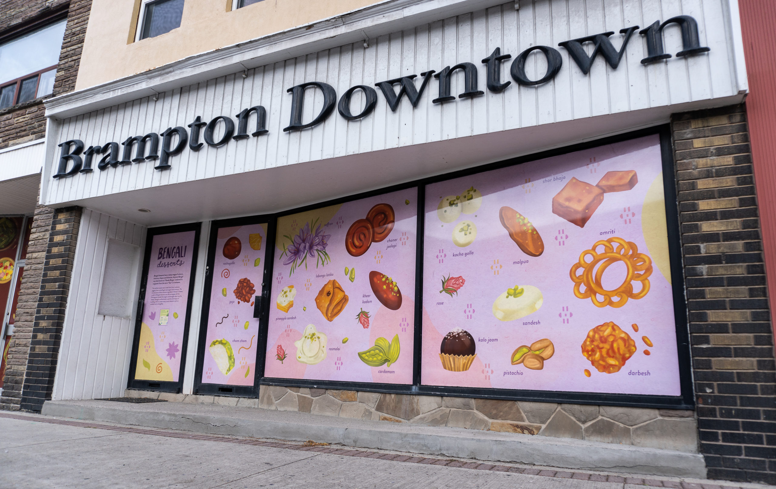 Photo of a Brampton storefront featuring the artwork of Meegan Lim that shows different Bengali sweets illustration on a lilac purple background.
