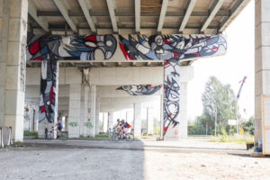 Mural by Fatspatrol underneath Toronto's Gardiner highway with cyclists biking by underneath