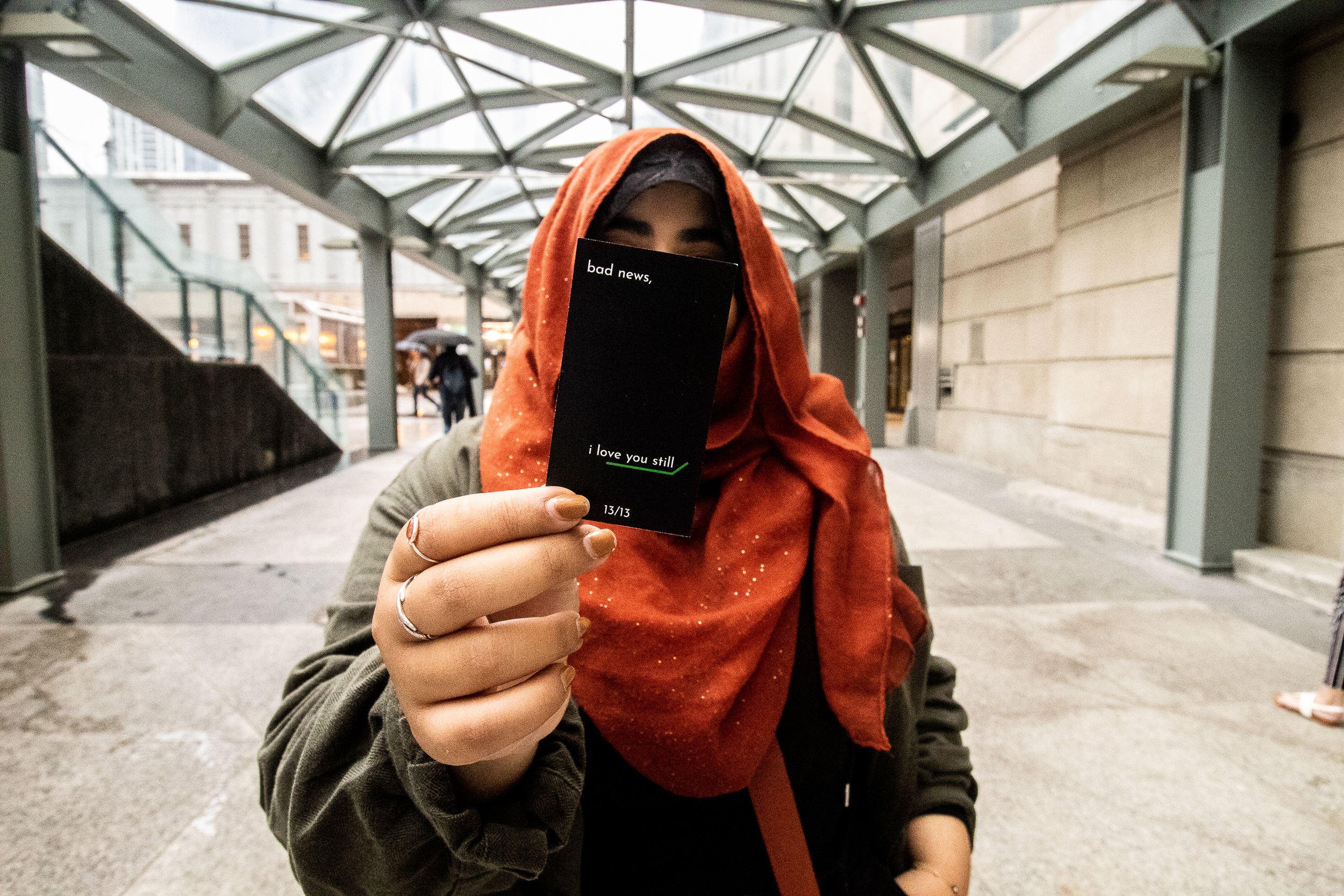 Photo of Yasmeen Nematt Alla holding up a black card with white text reading "bad news, i love you still"