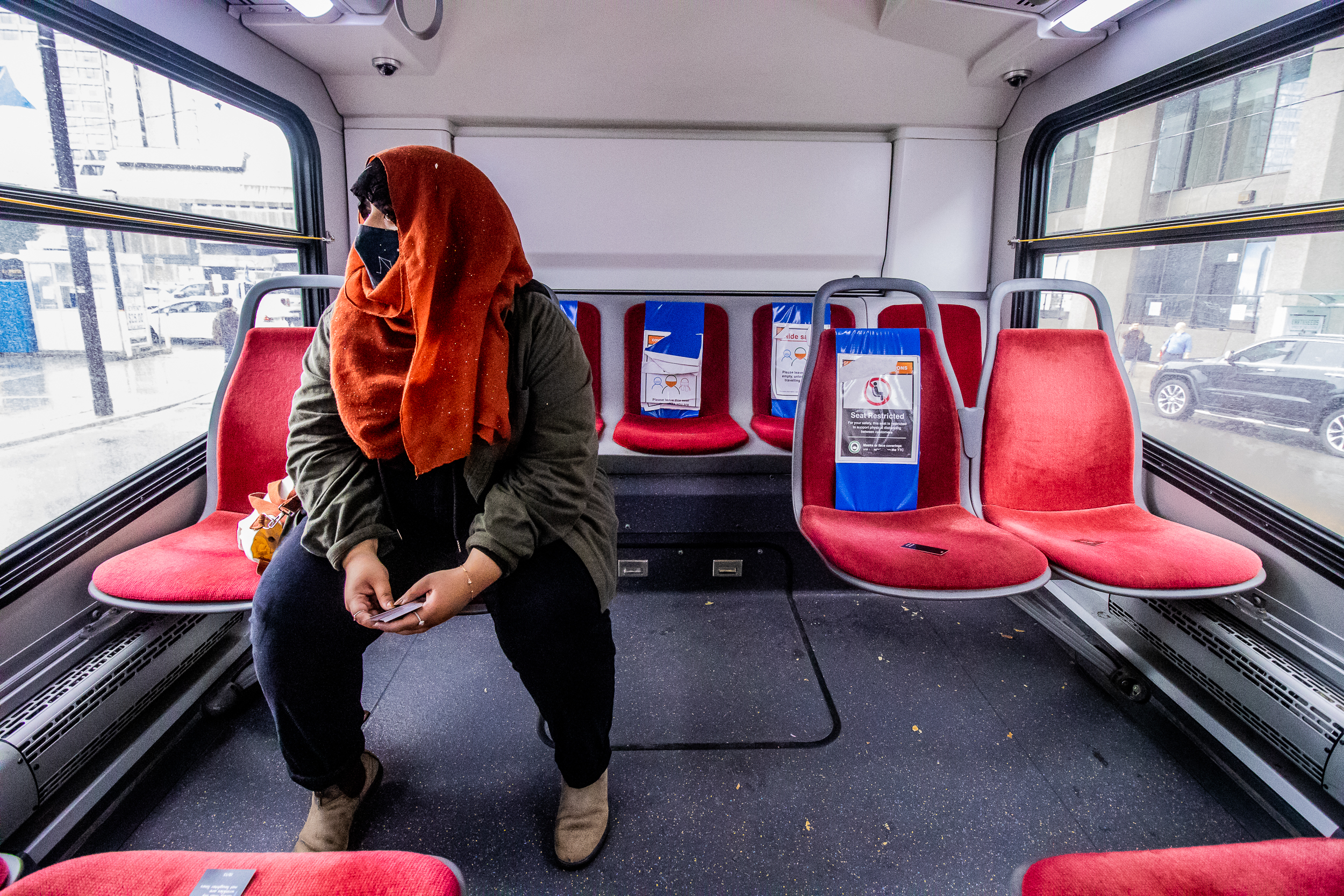 Photo of Yasmeen Nematt Alla sitting on the back of a TTC bus, the seats are red with some blue signs for social distancing.