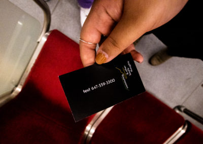 Photo of a hand holding a black card with white text that reads "text 647-559-3300, community and other lonely thoughts" on a TTC subway