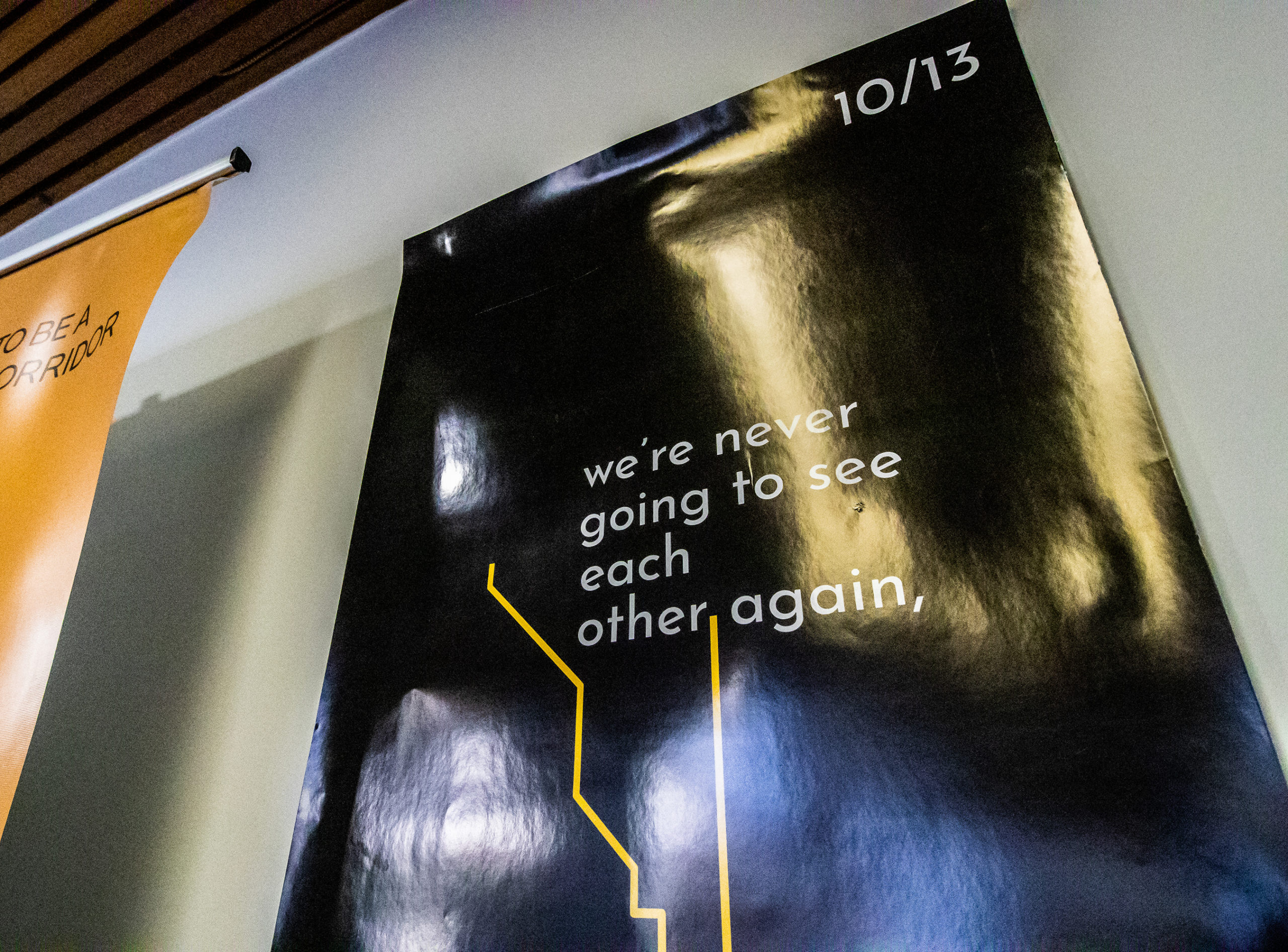 photo of a poster on a grey wall, taken from a low angle. It's background is black, with white text that reads "we're never going to see each other again" with a yellow subway line.