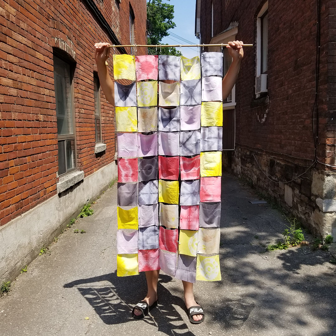 Person holding a hand- made quilt in an alley between two buildings.