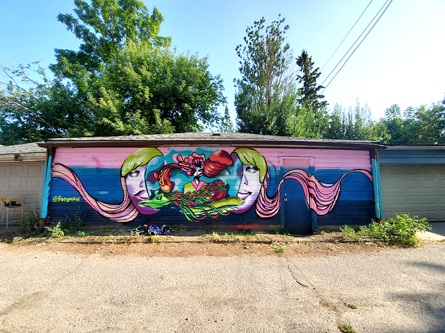 Photograph of a mural painted on the side of a house by Enna Kim. It features imagery of a face split in half with floral and abstract patterns in the centre set against a blue and pink background.