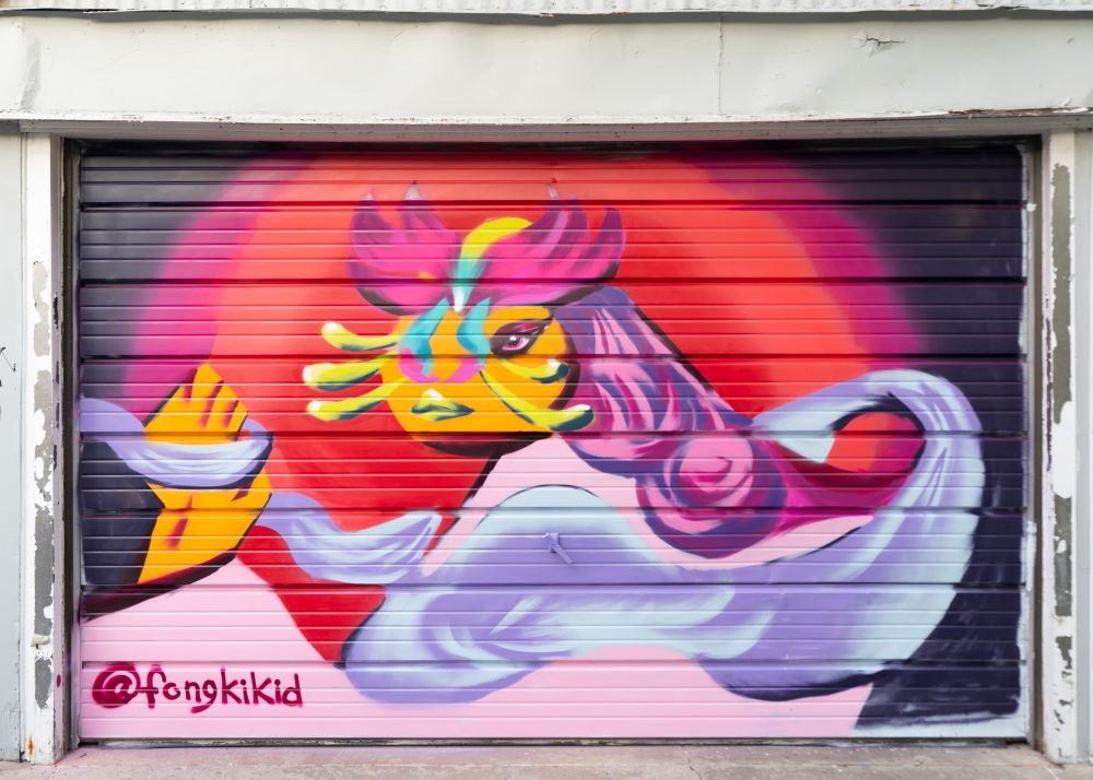 Photograph of a colourful garage door mural painted by Enna Kim. It features imagery of an abstract figure with the centre with an orange face and pink and purple hair.