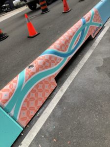 Section form a bike path painted with a dark and light pink pattern, including wavy lines of turquoise and blue.