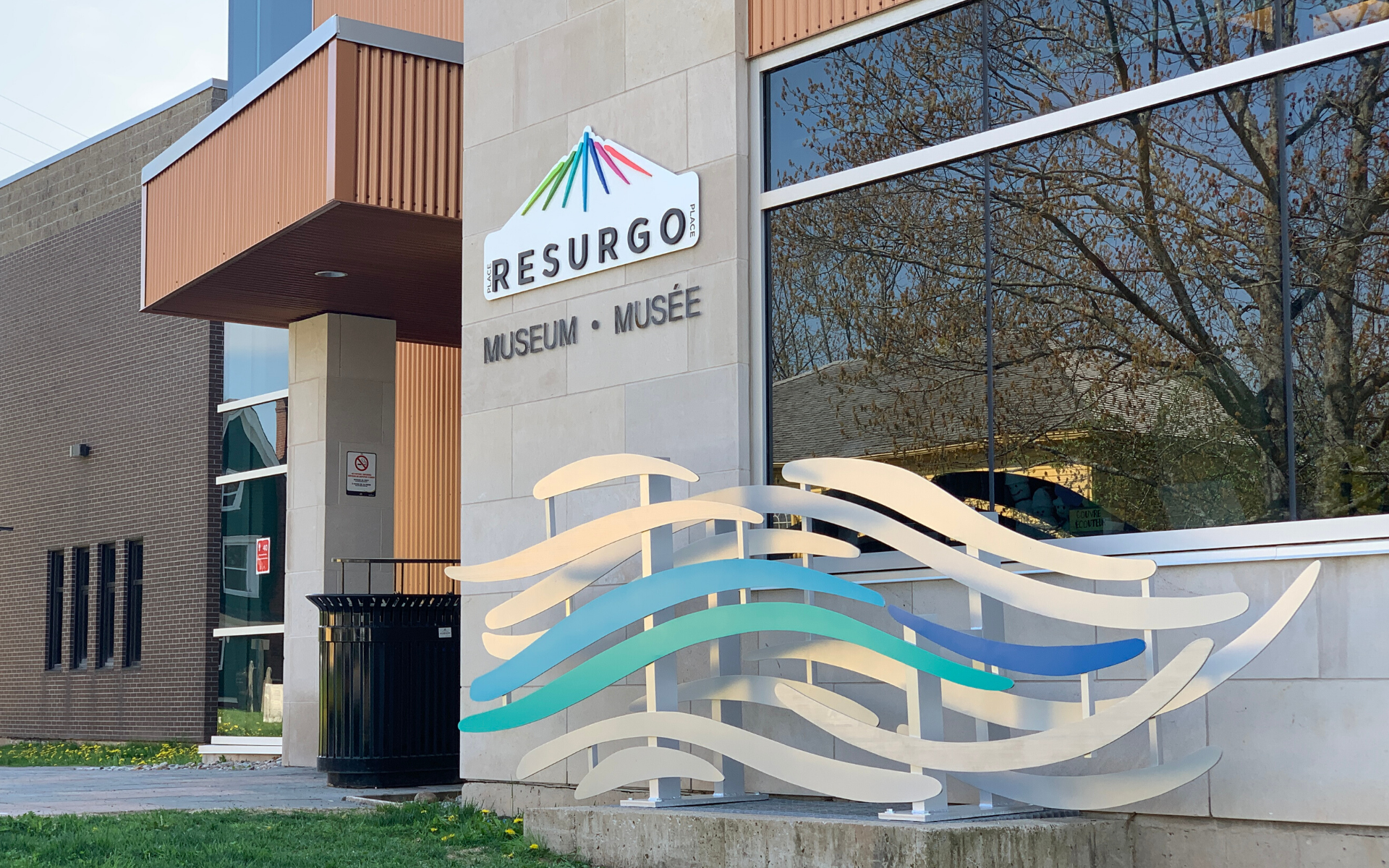 A sculptural work installed outside the Resurgo Place in Moncton, New Brunswick, Canada, consists of multiple wave-like shapes, one of which is turquoise, blue, and light blue.