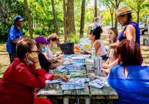 Community members sitting around a picnic table in Panorama Park and creating artwork as part of a community workshop by STEPS Public Art.