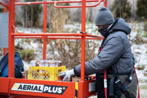 Close-up of an artist bundled up in warm clothes and safety equipment to operate a crane. They are going through supplies for a mural production.