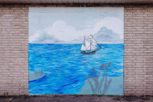 Outdoor mural by Jocelyn Kearns of a boat sailing away in a vast body of water