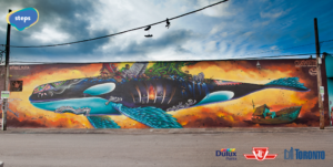 Large public art mural of a whale with different symbols of migration and immigration