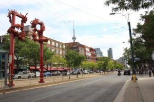 Photo of downtown Toronto Chinatown, two red poles with dragons, streetcar platform, trees and storefronts