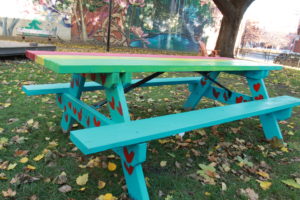Blue painted picnic table mural with red hearts. The tabletop has painted red, yellow and green stripes
