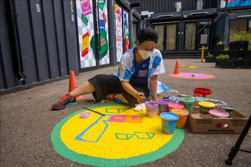 Amanda Lederle sitting on the ground and painting a colourful yellow and green ground mural at Stackt Market in Toronto