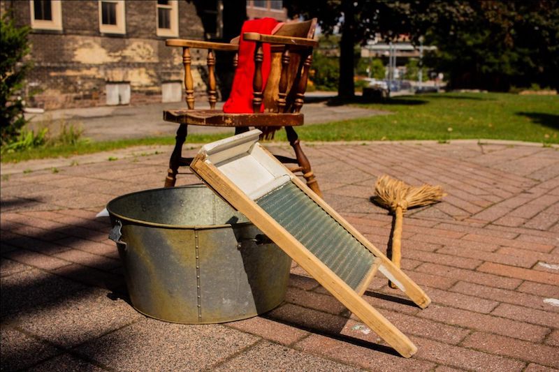 Charmaine Lurch's performance props for I am Lucie, I am Thornton. There is an old wooden chair, a tin bucket, and a washboard and broom