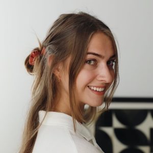 Madison Kennedy looking over her shoulder and smiling at the camera. She has long brown hair with a her hair tied in a half updo.