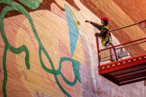 Wenting Li on a scissor lift and painting a large mural in Toronto's Chinatown