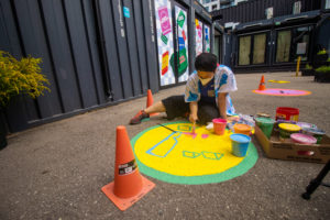 Amanda Lederle sitting on the ground and painting a colourful yellow and green ground mural at Stackt Market in Toronto