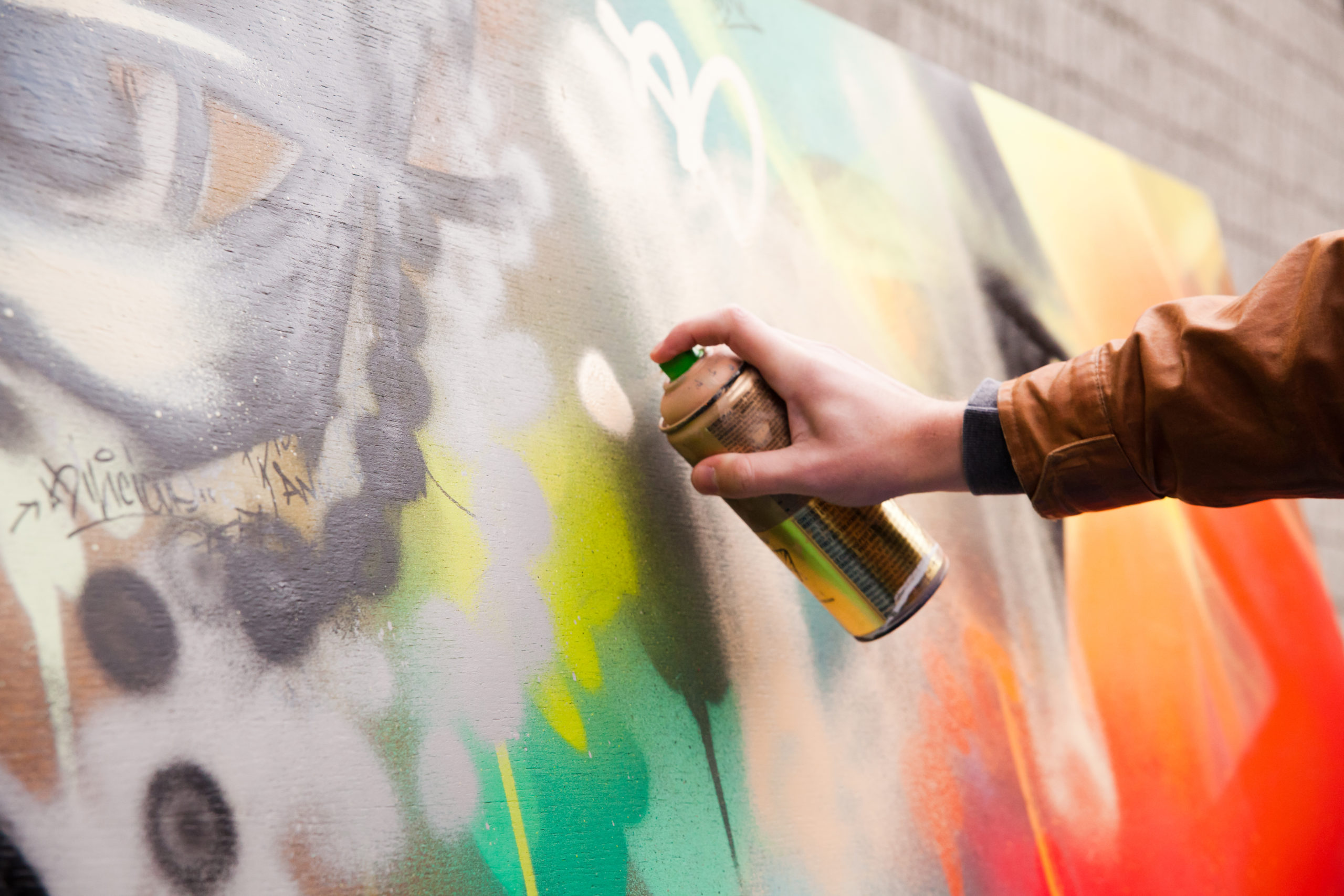 Photo of a arm holding a spray paint can painting a mural with colours of green, orange and yellow