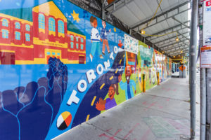 Shot of illustrated mural on a hoarding exhibit featuring the title "Toronto" and various city components