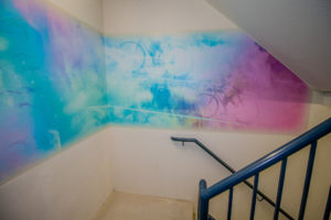 Close view of pink, purple and blue stairwell mural featuring overlaid images