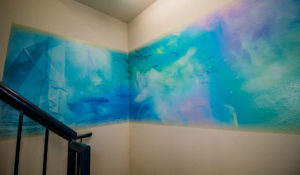 A digital mural in a stairwell of a building. It is blue with layered photographs and imagery resembling water and calmness