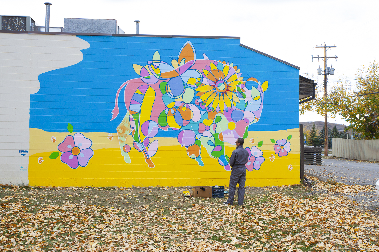 Bright blue and yellow mural by Bruno Canadien. The mural has vibrant imagery of a buffalo and florals with orange handprints