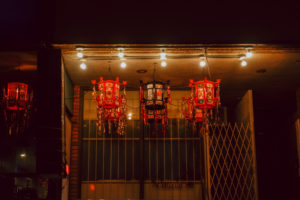 Photo of Yue Moon 2021 Exhibit of Lanterns with artwork, coloured red and black. It is taken at night and the lanterns illuminate a storefront.