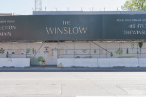 A hoarding exhibit for The Winslow development. The hoarding art stretches along a sidewalk with large pastel pink panels and dainty illustrations of plants, people walking, and buildings.