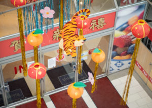 Photo take from above of a art installation in the atrium of Dragon City Mall with red and orange lanterns, paper flowers, and a paper cut tiger.