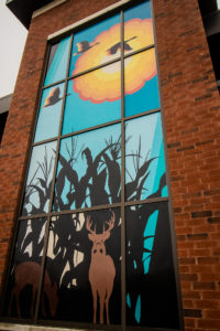 Vertical photo of a window detail on the Brampton Fire Station, the artwork has colours of teal, yellow and black with a silhouette of a deer.
