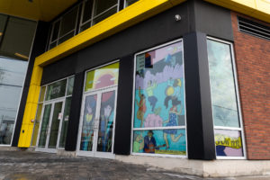 A storefront with the windows and glass doors painted with a colourful mural. Imagery showcases nature, flowers, and community to represent growth and community.