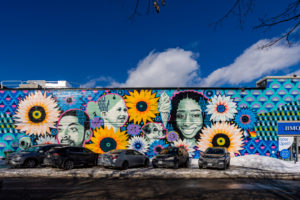 Outdoor mural on side of building with images of faces, patterns and flowers