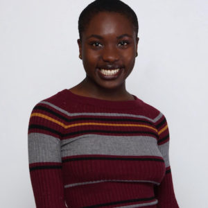 Jasmin-Nicole smiling at the camera against a white background. She is a Black artist and is wearing a long red long sleeve with orange and grey stripes.