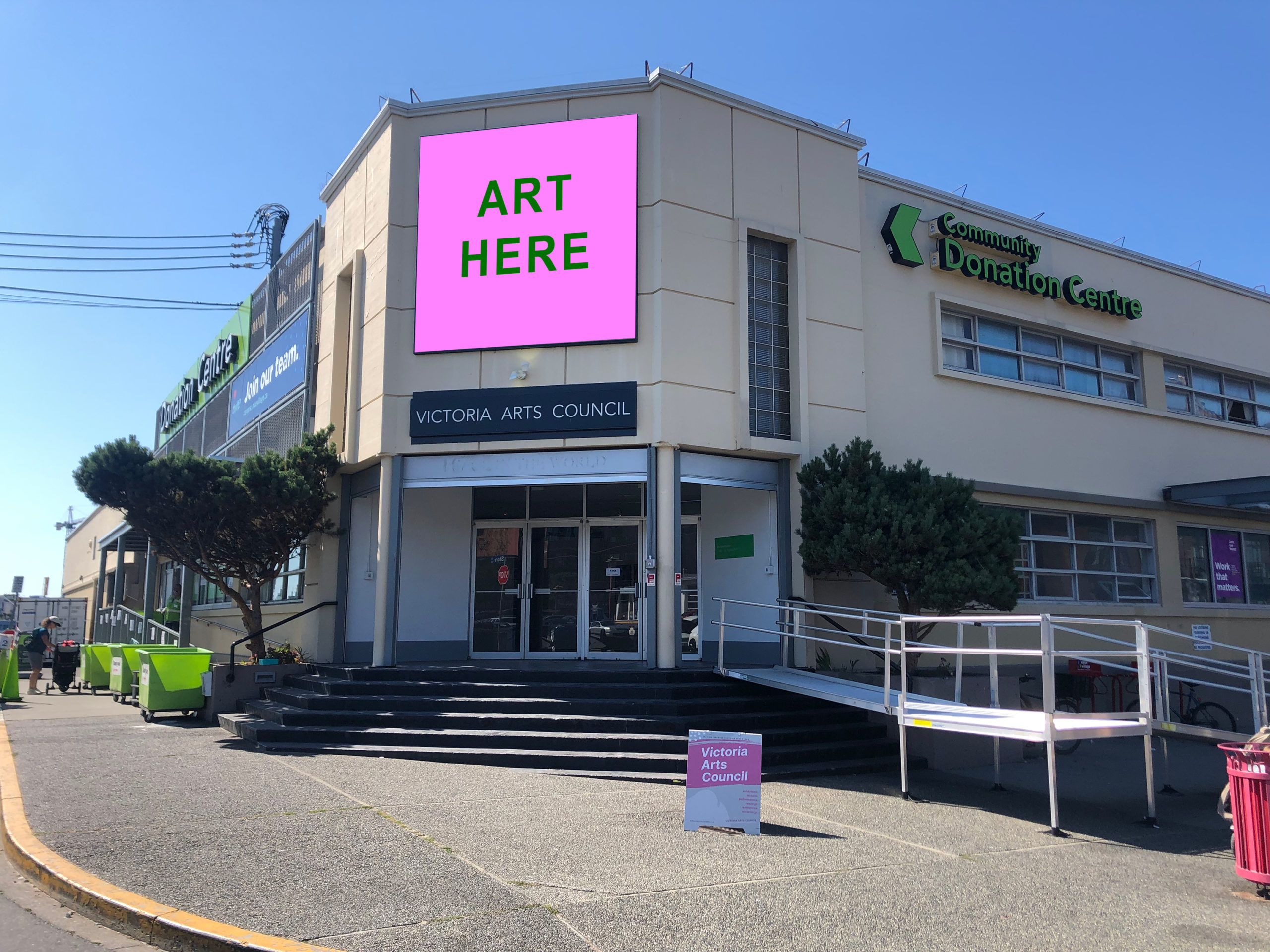 The Victoria Arts Council building on a sunny day with a mock-up of a billboard sign on that says "ART HERE" for a call to artists